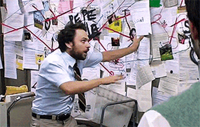 Charlie Day in a mailroom, arms spread, in front of a wall covered in papers and crisscrossed with red string